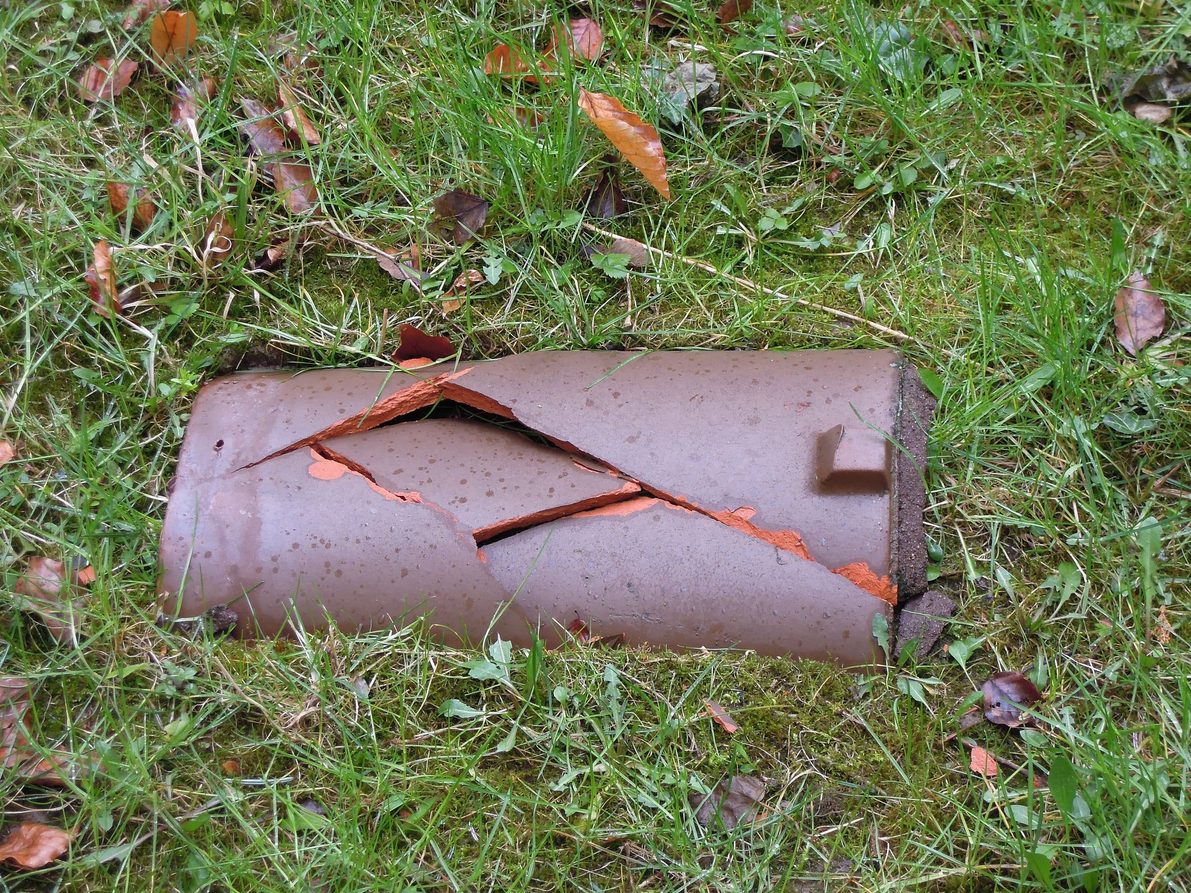 Cracked clay barrel roof tile lying in the grass after being blown off a roof in a storm