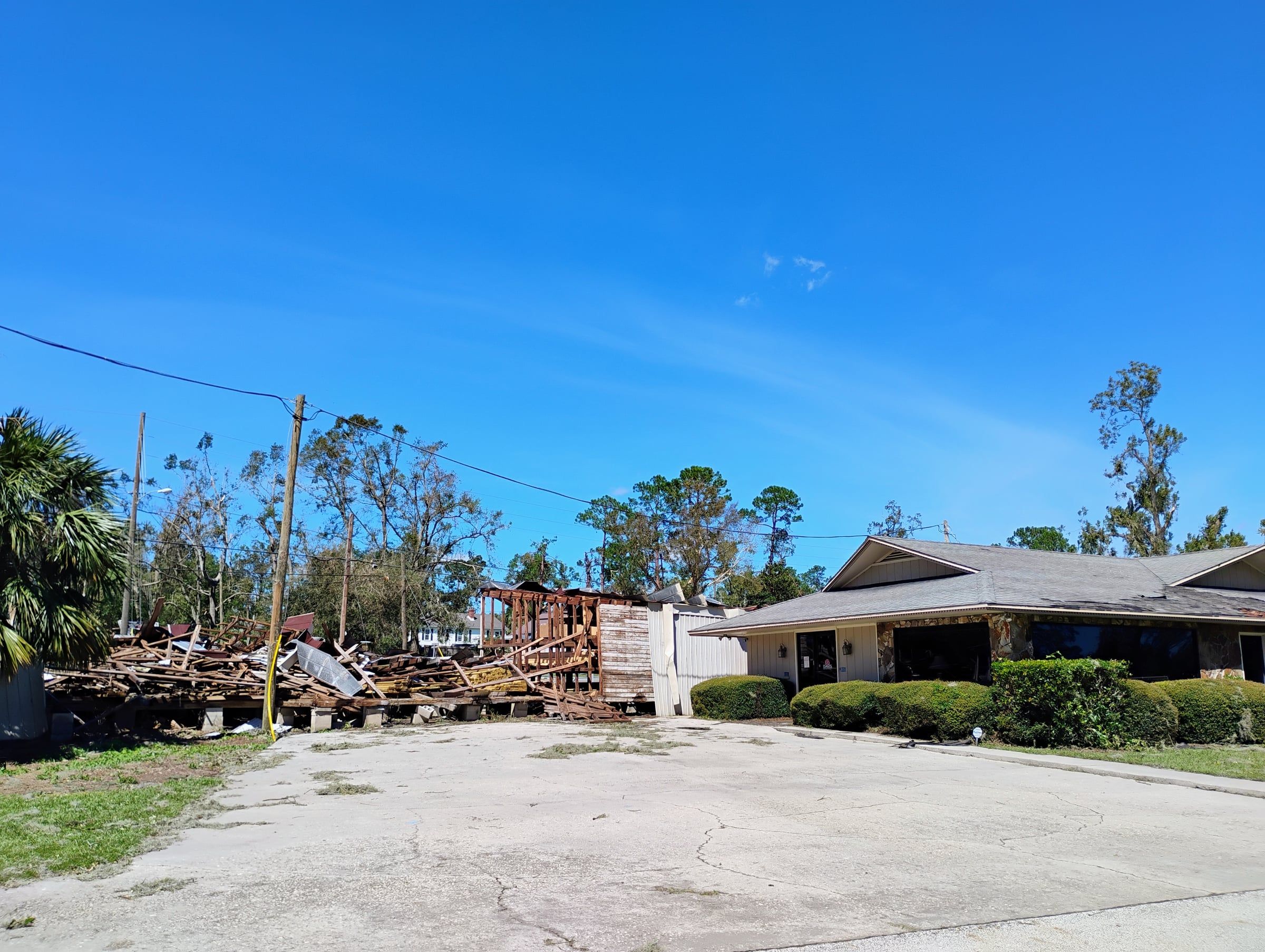Collapsed wood-frame building reduced to debris next to a single-story house with a damaged roof in Madison, Florida, after Hurricane Helene in 2024